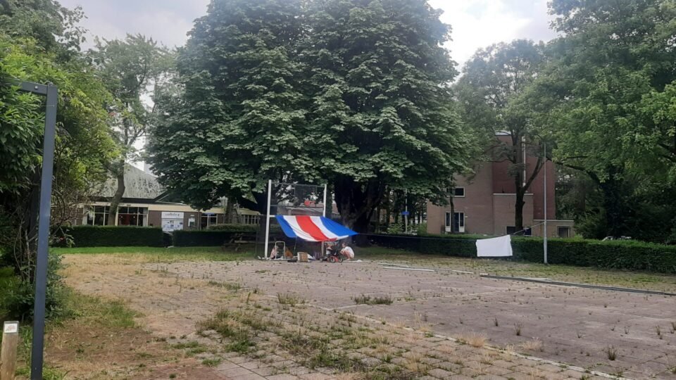 Een hut stalen voetbalgoal is met doeken in rood wit blauw (vlaggen?) omgetoverd tot een hut