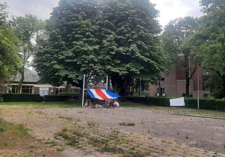 Een hut stalen voetbalgoal is met doeken in rood wit blauw (vlaggen?) omgetoverd tot een hut